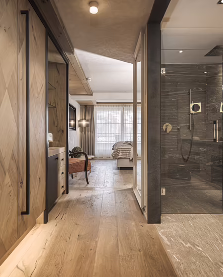Stilvoll entspannen in der Wohlfühlsuite Maya im Hotel Platzlhof Ein moderner Flur mit Holzfußboden, großen Fenstern und einer gläsernen Dusche im Badezimmer