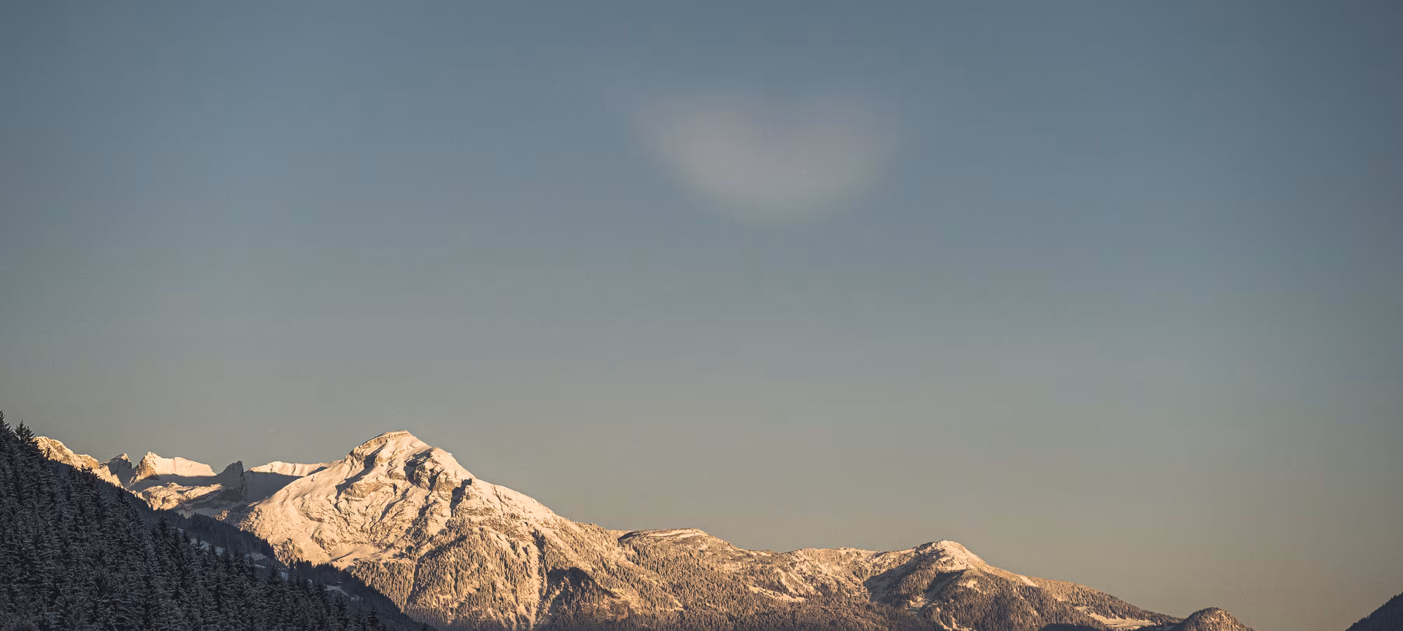 Aussicht auf verschneite Berge im Winter © mood.at Schneebedeckte Berge unter einem klaren Himmel, mit sanften Schatten und einem subtilen Farbverlauf am Horizont.